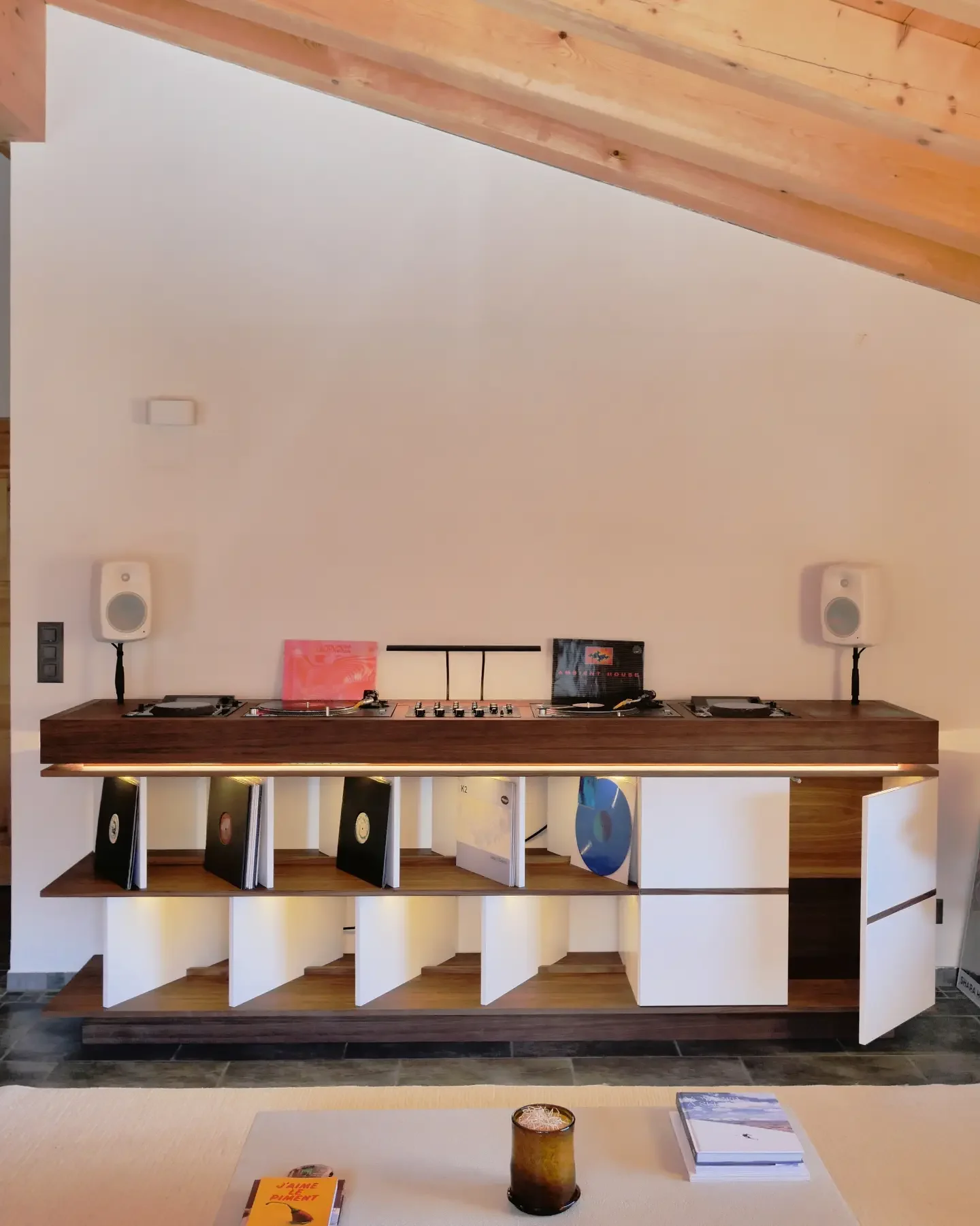 Cabine DJ en noyer et blanc sous une charpente en bois, avec platines, table de mixage et bacs à vinyles éclairés
